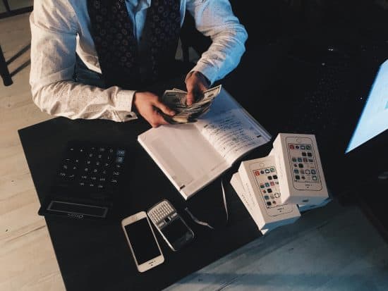 Man counting money with iPhones on desk