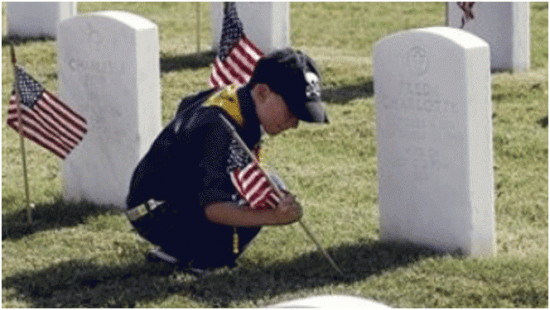 boy scout placing America flag at tombstones