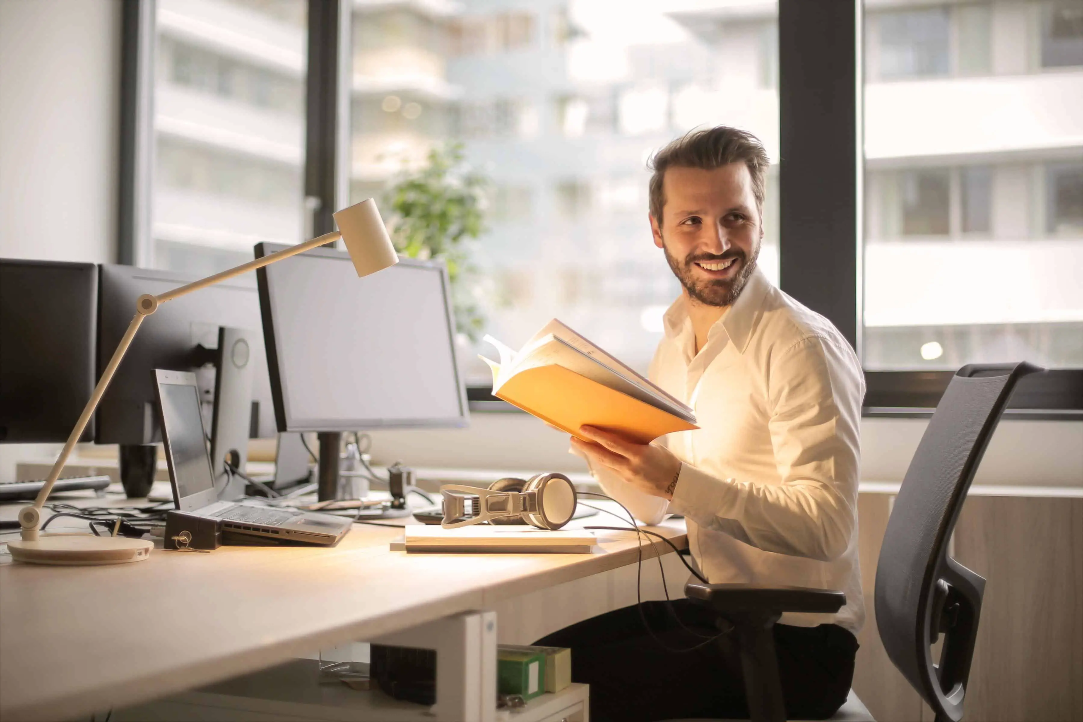 Smiling man sitting at a desk while holding a book