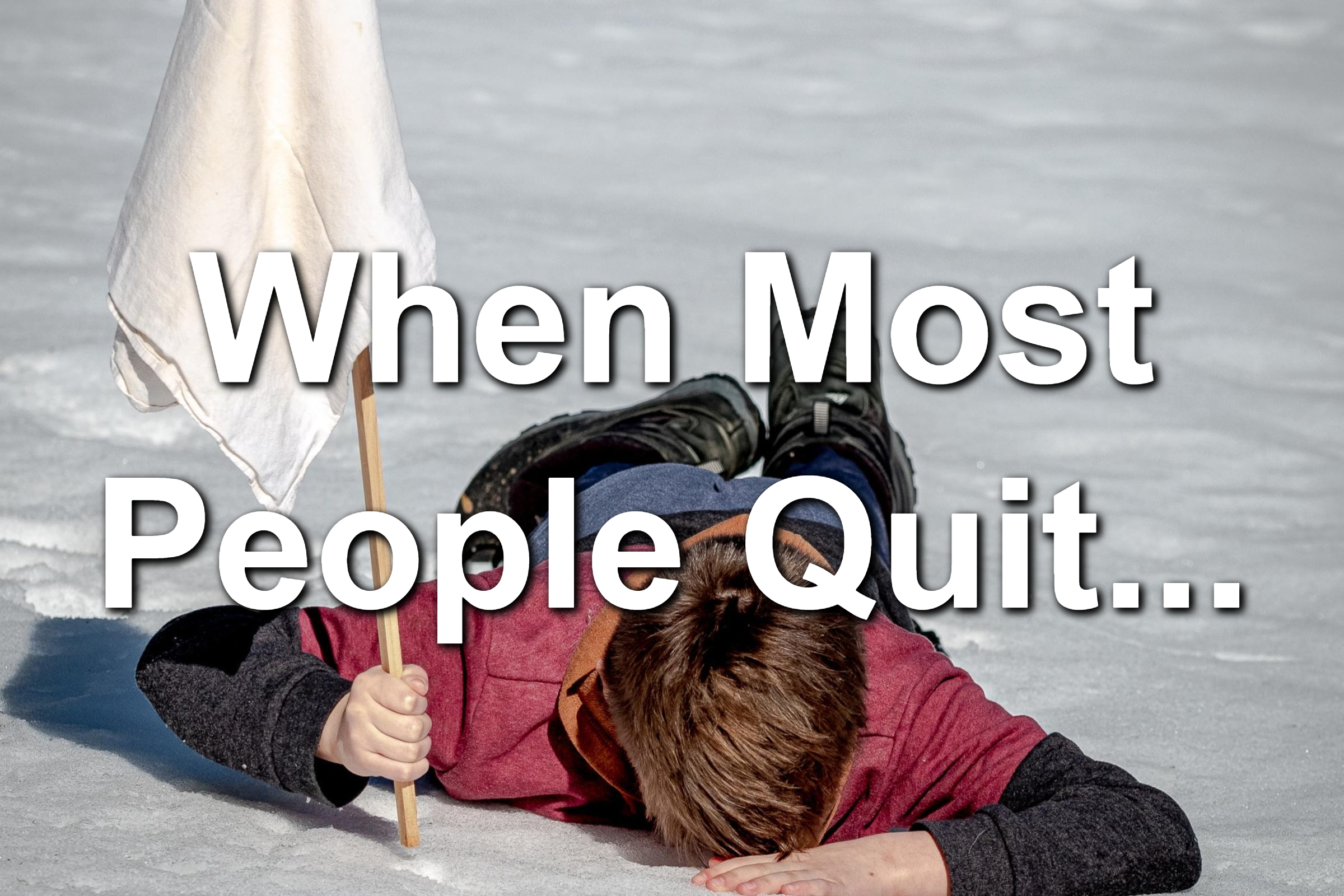 Young boy laying in the snow. He is holding a white flag