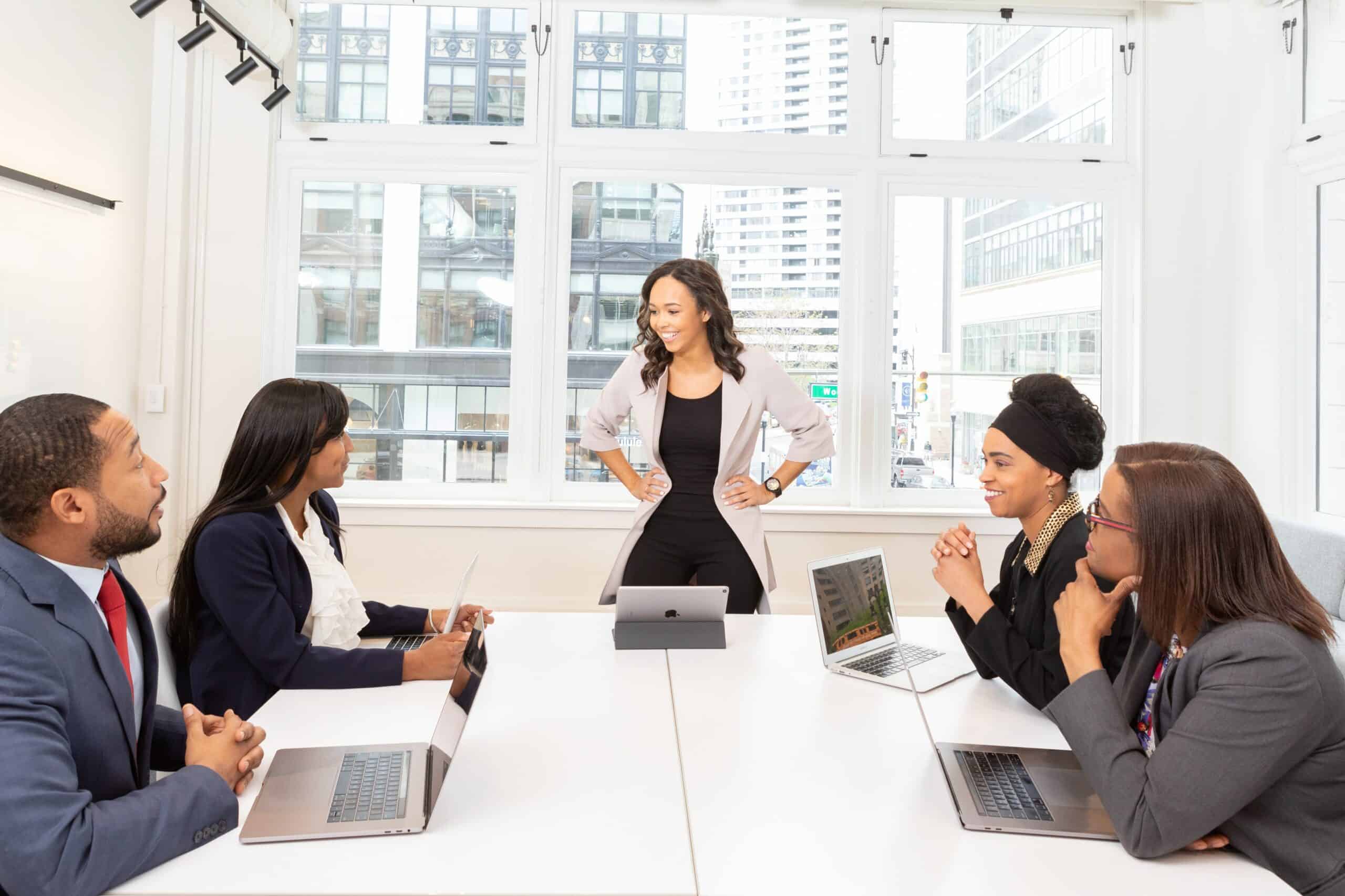 Woman standing with her hands on her hips addressing a room of people on their laptops