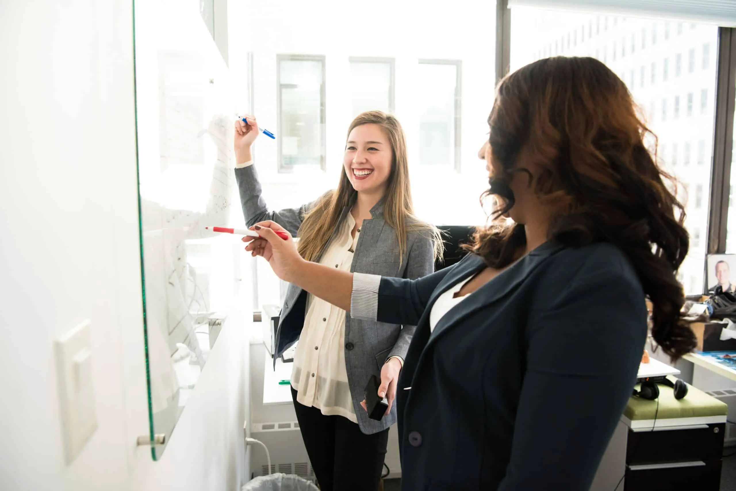 Two women in front of a whiteboard, smiling