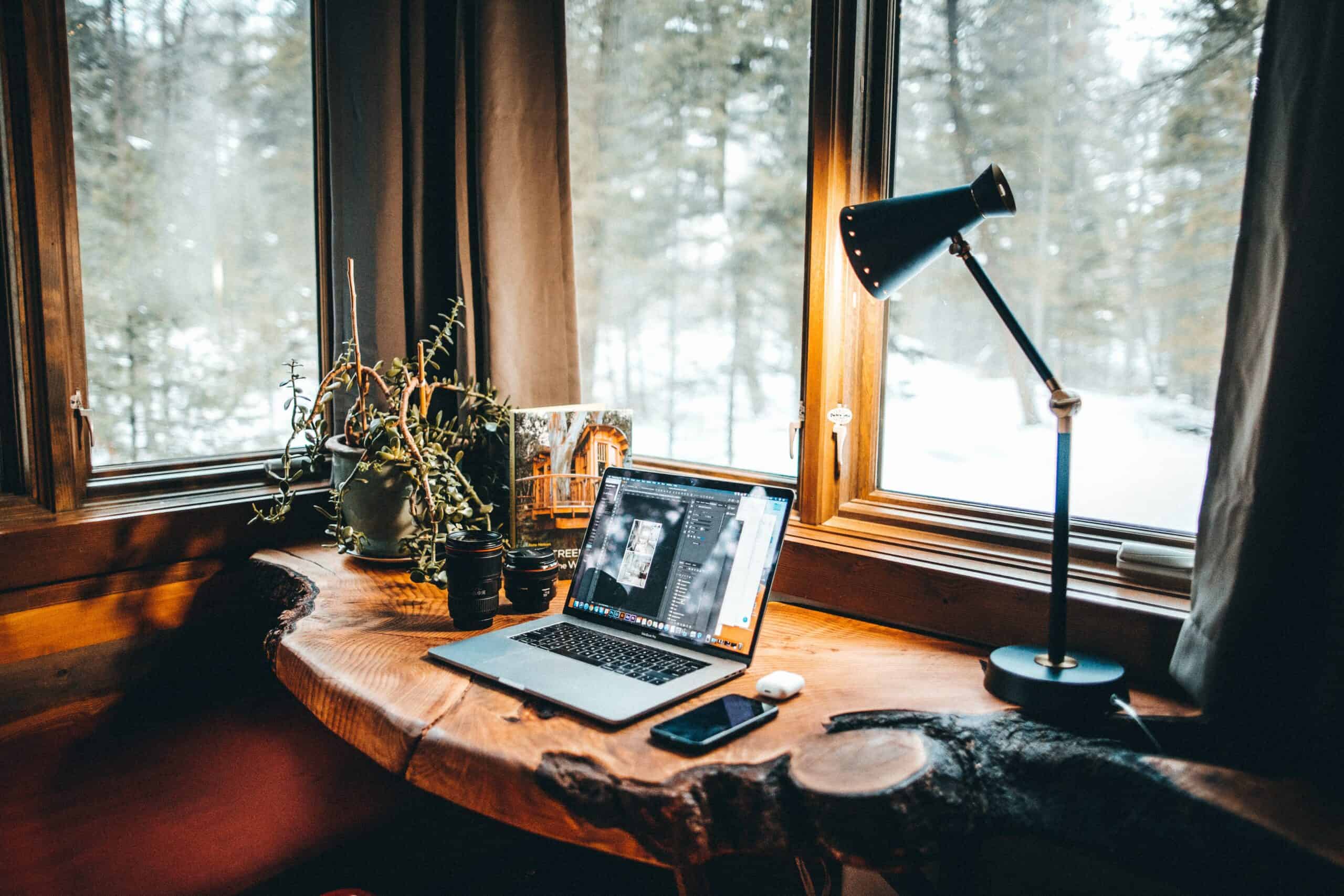 Laptop and cell phone sitting on a live-edge wooden desk. Light shining down on the desk.