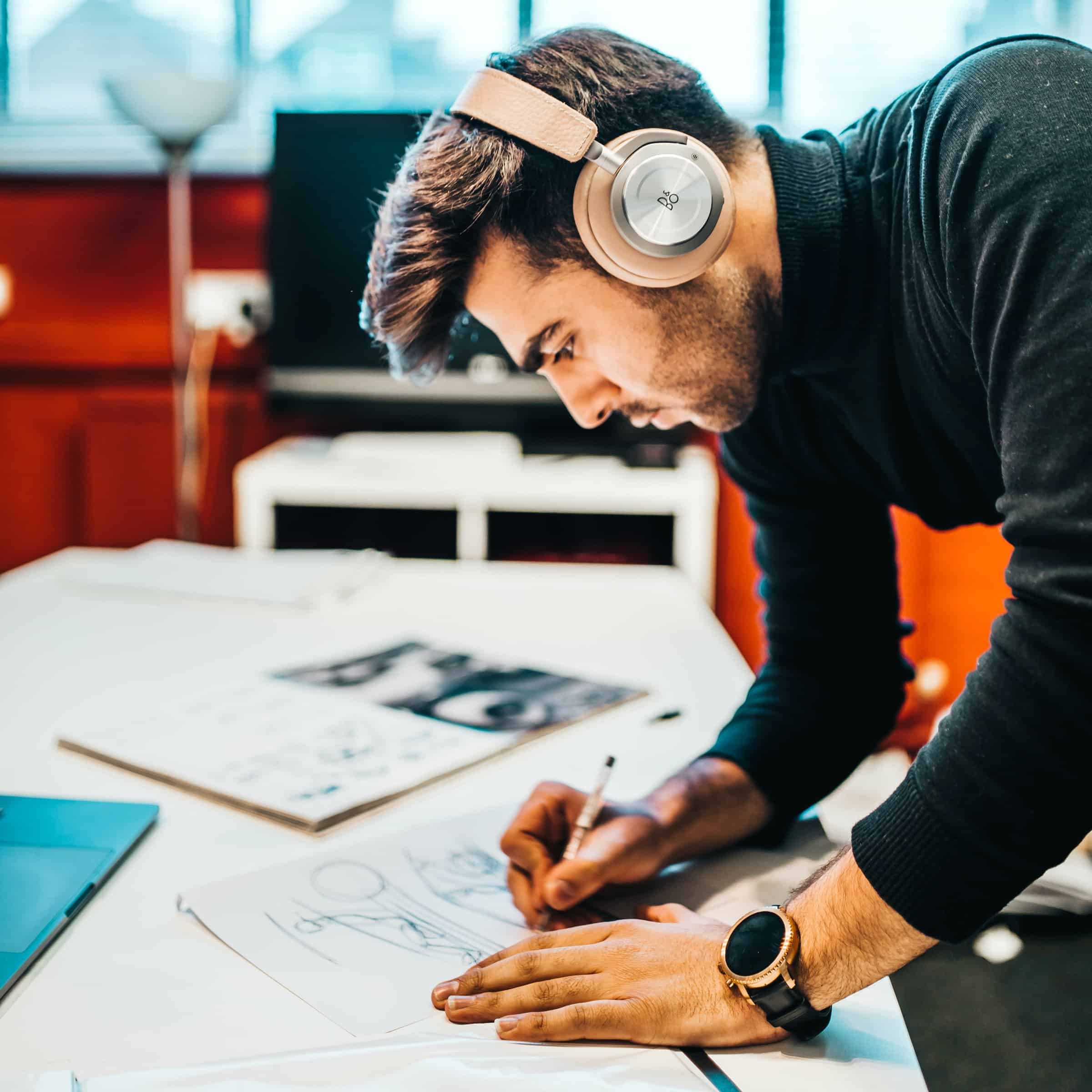 Man wearing headphones. Leaning over desk, sketching.